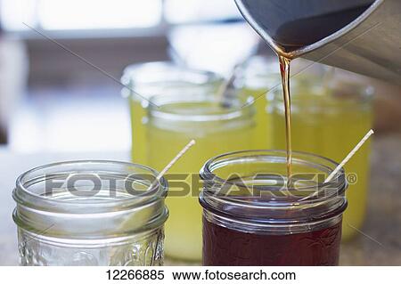 Stock Photography - A pitcher is used to pour hot soy wax into glass mason jars with candle wicks for the final step in candle making for home made gifts; Fort McMurray, Alberta, Canada. Fotosearch