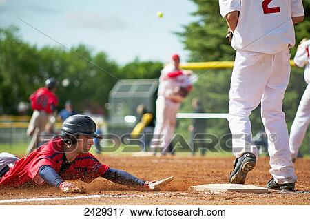 Stock Photo - A player slides into third base during a baseball tournament; Saskatoon, Saskatchewan, Canada. Fotosearch
