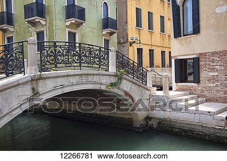 Stock Image - A quaint bridge over a small canal with colourful buildings; Venice, Italy. Fotosearch