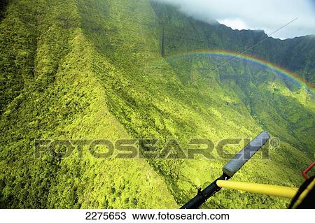 Stock Image - A rainbow across a steep green mountain face; Na Pali coast of Kauai, Hawaii, United States of America. Fotosearch
