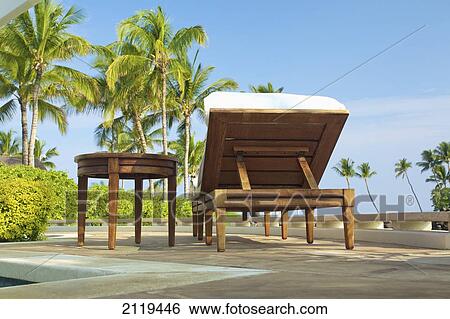Stock Photograph - A reclining chair and table sit on a patio with a view of palm trees; Hawaii, United States of America. Fotosearch