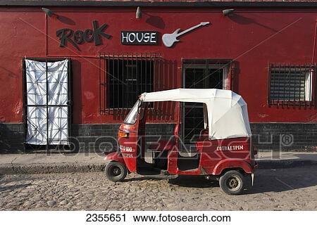 Stock Image - A Red Building With A Sign For Rock House And A Red Motor Cab Sitting Outside; Copan, Honduras. Fotosearch