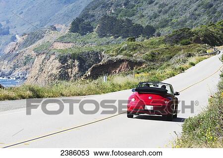 Stock Image - A red convertible traveling down the highway along the ocean; California, United States of America. Fotosearch