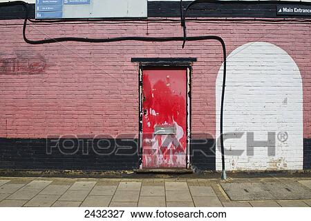 Stock Photo - A red door with peeling paint on a painted brick building; London, England. Fotosearch