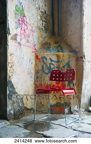 Stock Photo - A red plastic chair sits beside a weathered wall with spray painted graffiti; Barcelona, Spain. Fotosearch