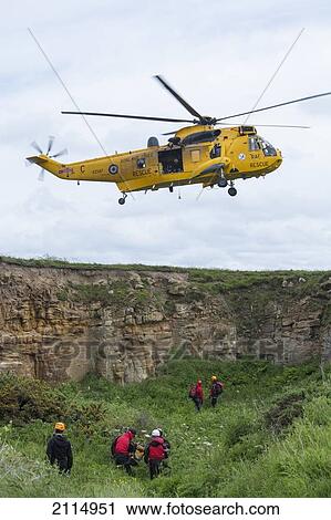 Stock Image - A Rescue Helicopter Flies Above Workers On The Ground; Northumberland England. Fotosearch