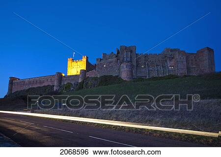 Stock Photograph - A Road Beside Bamburgh Castle Illuminated At Dusk; Bamburgh Northumberland England. Fotosearch