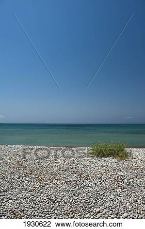 Stock Image - A rock beach along the water's edge with a view of blue sky against the horizon; Ibiza, Spain. Fotosearch