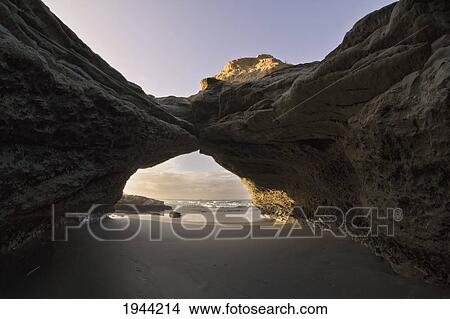 Picture - A Rock Formation Forms An Arch On The Beach With A View Of The Ocean; Cape Foulwind South Island New Zealand. Fotosearch