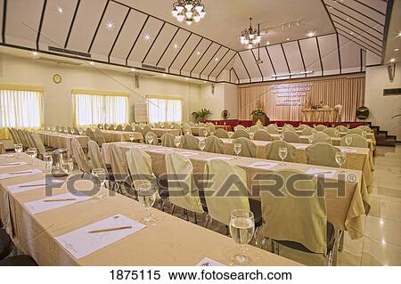 Stock Photography - A Room Set Up With Tables And Chairs In A Row Facing A Platform. Fotosearch