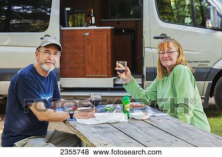 A Senior Couple Sit At A Picnic Table Eating Dinner With Their Camper Van In The Background At West Canada Creek Campsites; Poland, New York, United States Of America View Large Photo Image Stock Photo - A Senior Couple Sit At A Picnic Table Eating Dinner With Their Camper Van In The Background At West Canada Creek Campsites; Poland, New York, United States Of America. Fotosearch