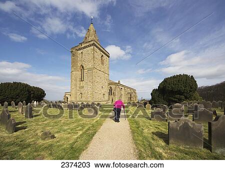 A senior woman walks with a cane up a path beside a cemetery towards a church; Staithes, North Yorkshire, England View Large Photo Image Stock Image - A senior woman walks with a cane up a path beside a cemetery towards a church; Staithes, North Yorkshire, England. Fotosearch
