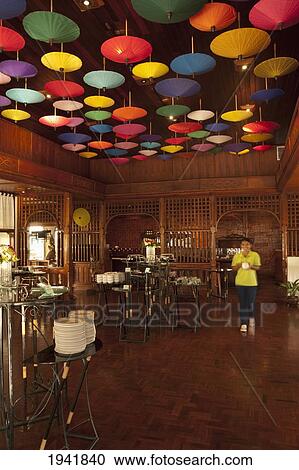 Stock Image - A Server Walks Under Umbrellas Hanging From The Ceiling At The Restaurant In Amari Rincome Hotel; Chiang Mai Thailand. Fotosearch