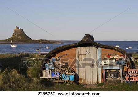Stock Image - A shed with fishing equipment at the water's edge with a view of Lindisfarne Castle on Holy Island; Lindisfarne, Northumberland, England. Fotosearch