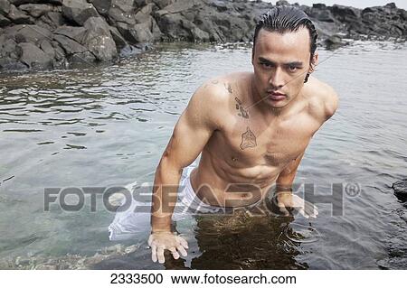 Stock Image - A shirtless man on a rock ledge in the water; Honolulu, Oahu, Hawaii, United States of America. Fotosearch