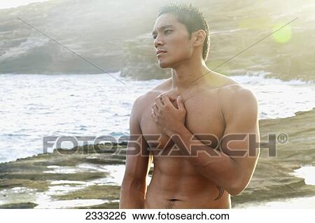 A shirtless man standing on the shore at the water's edge; Oahu, Hawaii, United States of America View Large Photo Image Stock Photograph - A shirtless man standing on the shore at the water's edge; Oahu, Hawaii, United States of America. Fotosearch