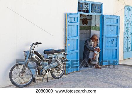 Stock Image - A Shopkeeper Enjoys An Afternoon Nap In The Doorway Of His Shop; Tunisia, North Africa. Fotosearch