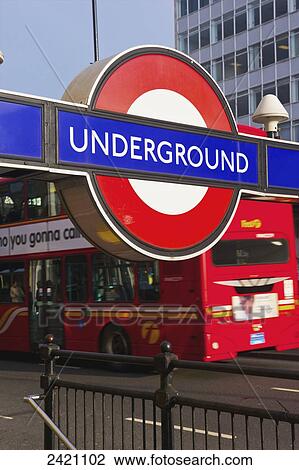 Stock Image - A sign for the steps to go underground beside a street with a double decker bus going by; London, England. Fotosearch