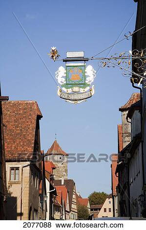 Stock Photo - A Sign Hanging From A Building Against A Blue Sky; Rothenburg Ob Der Tauber Bavaria Germany. Fotosearch