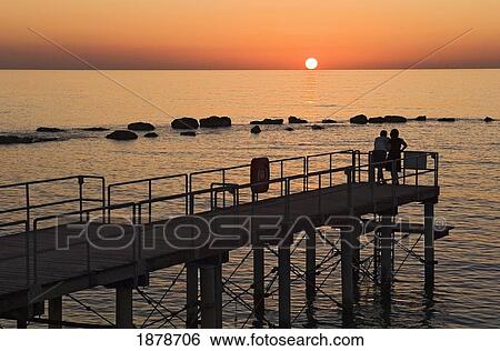 A Silhouetted Couple Watch The Sun Setting Out At Sea View Large Photo Image Stock Photograph - A Silhouetted Couple Watch The Sun Setting Out At Sea. Fotosearch