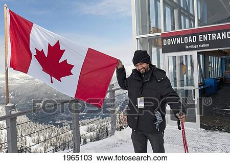 Stock Image - A Skiier Holds Up A Canadian Flag On A Balcony At A Ski Resort; Whistler British Columbia Canada. Fotosearch