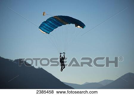 A skydiver floats with a parachute against a blue sky and the swiss alps; Locarno, Ticino, Switzerland View Large Photo Image Stock Photo - A skydiver floats with a parachute against a blue sky and the swiss alps; Locarno, Ticino, Switzerland. Fotosearch