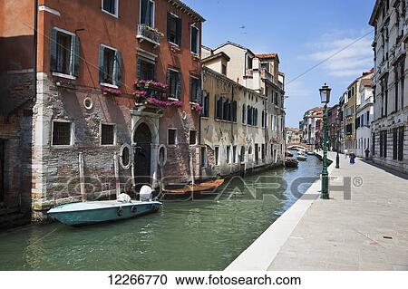 Stock Image - A small canal with boats and lamp posts lining the walkway; Venice, Italy. Fotosearch