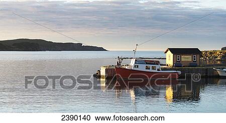 Stock Image - A small fishing boat sits on the tranquil water beside a pier; Twillingate, Newfoundland and Labrador, Canada. Fotosearch