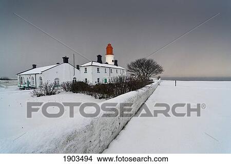 Picture - A Snow Covered Fence With A Lighthouse And Building In The Background; South Shields, Tyne And Wear, England. Fotosearch
