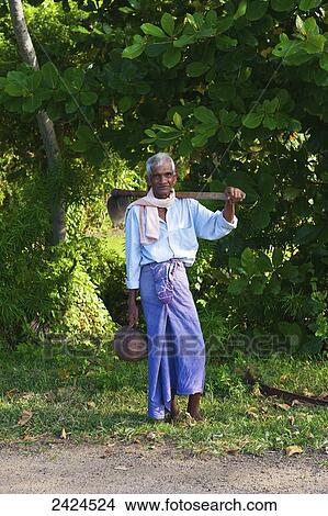 Picture - A Sri Lankan man standing at the side of a road with a shovel; Ulpotha, Embogama, Sri Lanka. Fotosearch