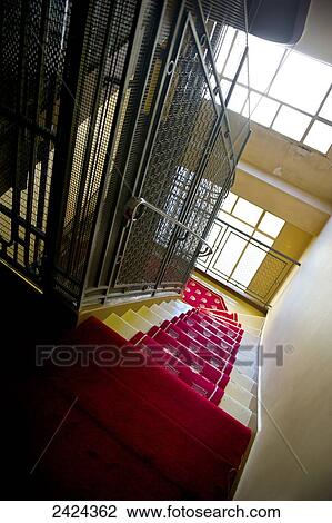 Stock Image - A stairway with red carpet and sunlight coming in the windows; Paris, France. Fotosearch