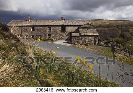 Stock Photograph - A Stone House On The Side Of A Road With Storm Clouds Overhead; Swaledale England. Fotosearch