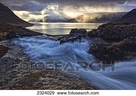 A stormy sky breaks above the Arnarfjorour fjord at sunset as waterfall Dynjandi flows into it; Iceland View Large Photo Image Stock Photo - A stormy sky breaks above the Arnarfjorour fjord at sunset as waterfall Dynjandi flows into it; Iceland. Fotosearch