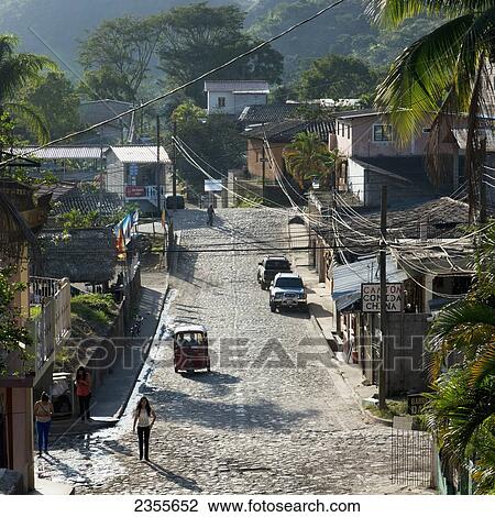 Stock Image - A Street With Pedestrians, Cars, Buildings And Lush Vegetation; Copan, Honduras. Fotosearch