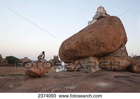 A structure sits atop a large boulder with a man sitting on a large rock next to it; Hampi, Karnataka, India View Large Photo Image Stock Image - A structure sits atop a large boulder with a man sitting on a large rock next to it; Hampi, Karnataka, India. Fotosearch