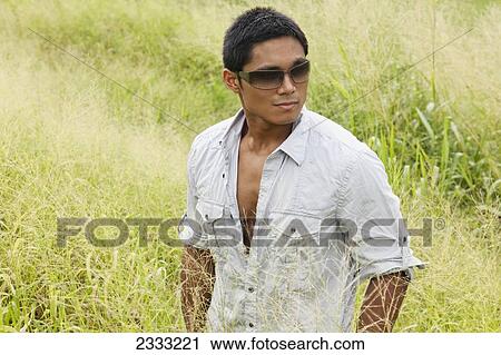 Stock Image - A stylish man standing in a grassy field; Hawaii, United States of America. Fotosearch