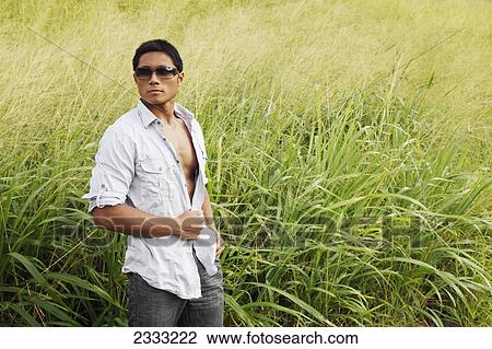 Stock Image - A stylish man standing in a grassy field; Hawaii, United States of America. Fotosearch