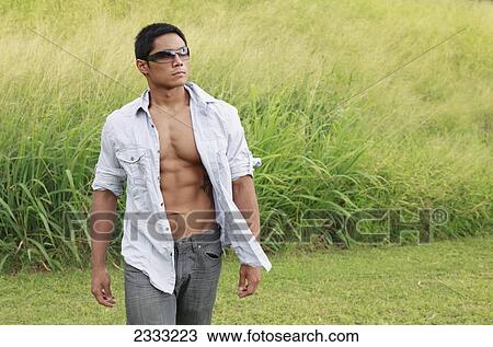 Stock Image - A stylish man walking in a grassy field; Hawaii, United States of America. Fotosearch