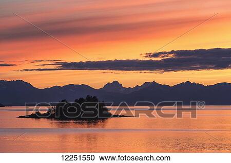 Stock Image - A summer sunset colours the sky adjacent to Lynn Canal, with Chilkat Mountains in the distance; Alaska, United States of America. Fotosearch