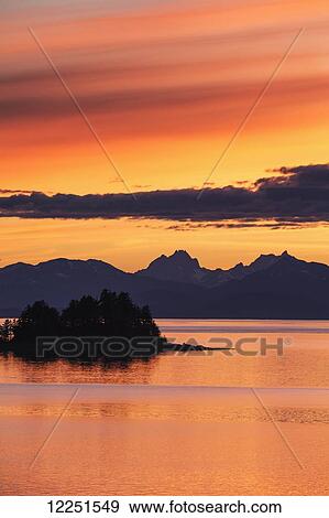 A summer sunset colours the sky adjacent to Lynn Canal, with Chilkat Mountains in the distance; Alaska, United States of America View Large Photo Image Stock Photo - A summer sunset colours the sky adjacent to Lynn Canal, with Chilkat Mountains in the distance; Alaska, United States of America. Fotosearch