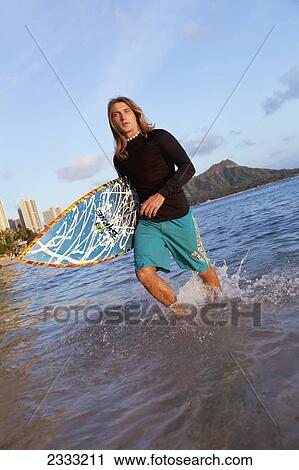 A surfer carrying his surfboard and walking in shallow water; Waikiki, Oahu, Hawaii, United States of America View Large Photo Image Stock Image - A surfer carrying his surfboard and walking in shallow water; Waikiki, Oahu, Hawaii, United States of America. Fotosearch
