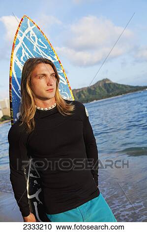 Stock Image - A surfer holding his surfboard at the water's edge; Waikiki, Oahu, Hawaii, United States of America. Fotosearch