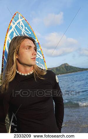 Stock Photo - A surfer holding his surfboard at the water's edge; Waikiki, Oahu, Hawaii, United States of America. Fotosearch