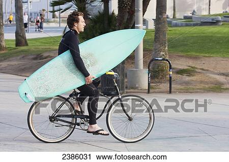 A surfer riding his bicycle and carrying his surfboard; California, United States of America View Large Photo Image Stock Image - A surfer riding his bicycle and carrying his surfboard; California, United States of America. Fotosearch