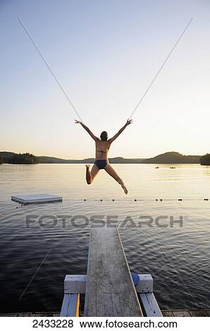 A swimmer jumps off a diving board as the sun sets over a lake in Muskoka; Huntsville, Ontario, Canada View Large Photo Image Stock Photo - A swimmer jumps off a diving board as the sun sets over a lake in Muskoka; Huntsville, Ontario, Canada. Fotosearch