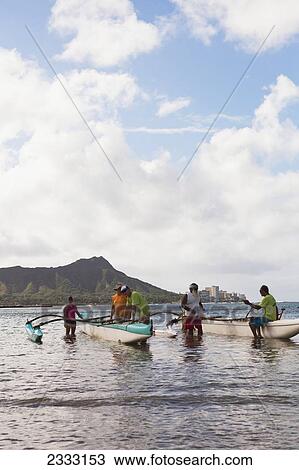 Stock Image - A team of locals prepare to set sail on an outrigger canoe; Oahu, Hawaii, United States of America. Fotosearch