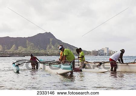 Stock Photograph - A team of locals prepare to set sail on an outrigger canoe; Oahu, Hawaii, United States of America. Fotosearch