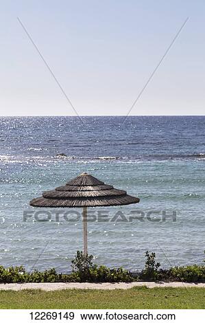 A thatched umbrella stands at the water's edge; Paphos, Cyprus View Large Photo Image Stock Photo - A thatched umbrella stands at the water's edge; Paphos, Cyprus. Fotosearch