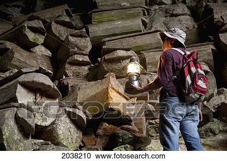 A Tour Guide Uses A Lantern To Look At The Many Coffins In The Entrance To Lumiang Burial Cave Near Sagada; Luzon Philippines View Large Photo Image Stock Image - A Tour Guide Uses A Lantern To Look At The Many Coffins In The Entrance To Lumiang Burial Cave Near Sagada; Luzon Philippines. Fotosearch