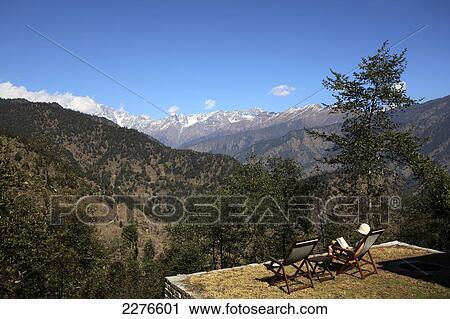 Stock Image - A tourist sits reading a book with a view of the Indian Himalayas; Uttaranchal, India. Fotosearch